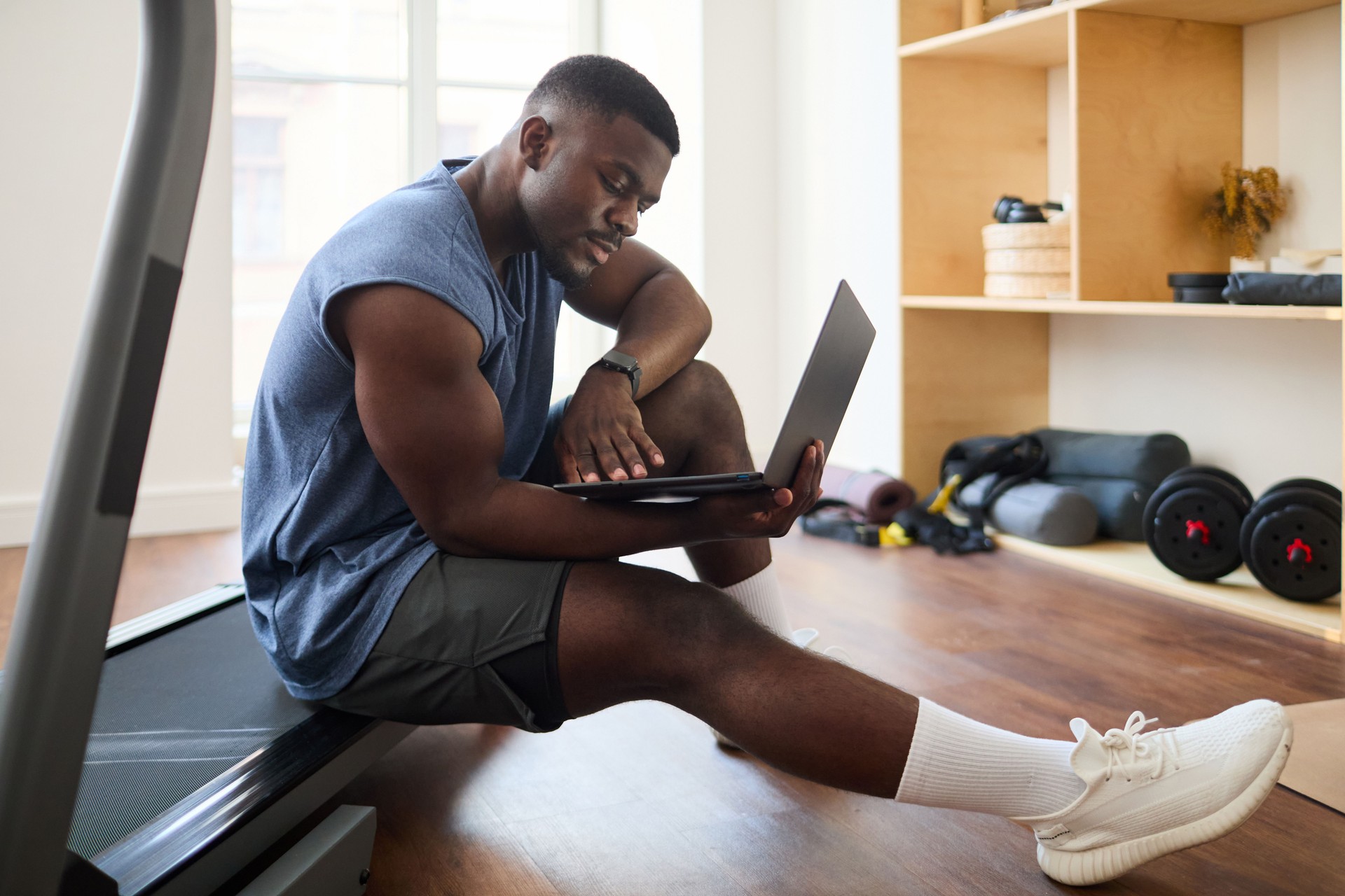 Man Using Laptop While Resting on Treadmill in Gym Setting